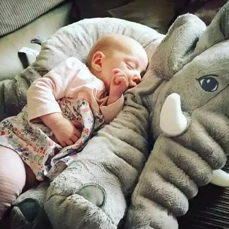 Baby in a light pink long sleeve top and floral dress, sleeping on a plush grey elephant pillow