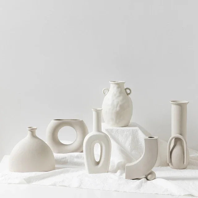 Minimalist off-white ceramic vases with modern geometric shapes on a white cloth background.