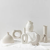 Minimalist off-white ceramic vases with modern geometric shapes on a white cloth background.