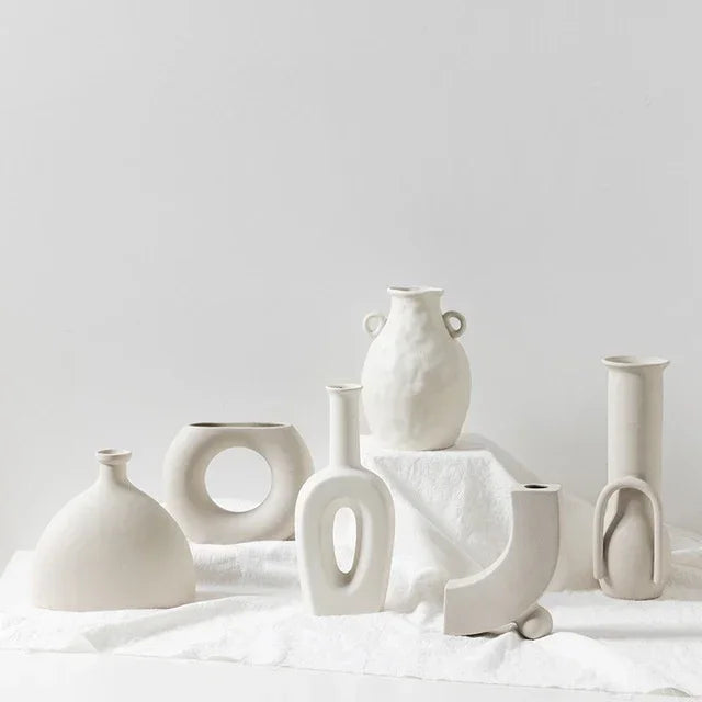 Minimalist off-white ceramic vases with modern geometric shapes on a white cloth background.
