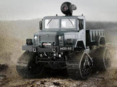 Gray off-road truck with tank treads and camera on roof driving across rugged terrain.