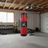 Red leather heavy punching bag with black accents hanging in a home gym setting
