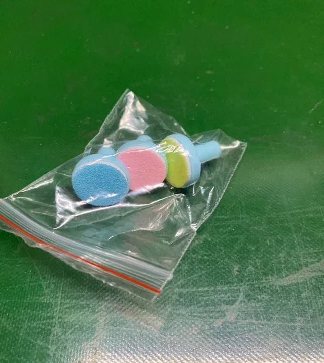 Pastel blue, pink, and yellow foam earplugs in a small plastic bag on green background