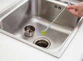 Hand using flexible drain cleaning tool to remove debris from stainless steel kitchen sink.