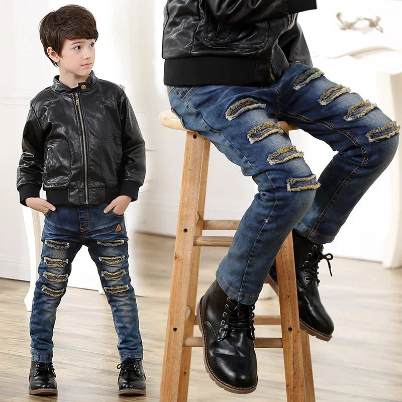Boy wearing black faux leather jacket and blue distressed skinny jeans with black boots