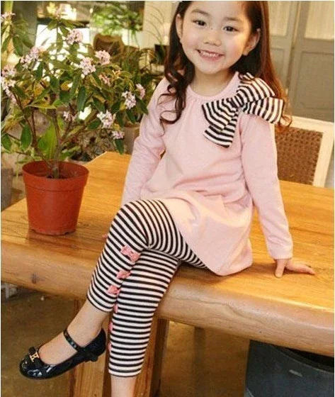 Girl in light pink long sleeve tunic with striped bow, and black striped leggings with bows