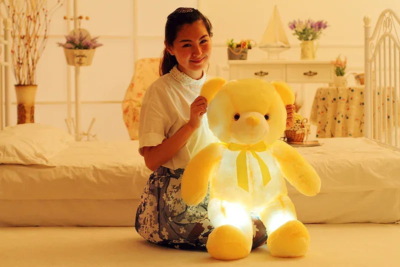 Woman in a white lace top and floral skirt with a large glowing yellow plush teddy bear.
