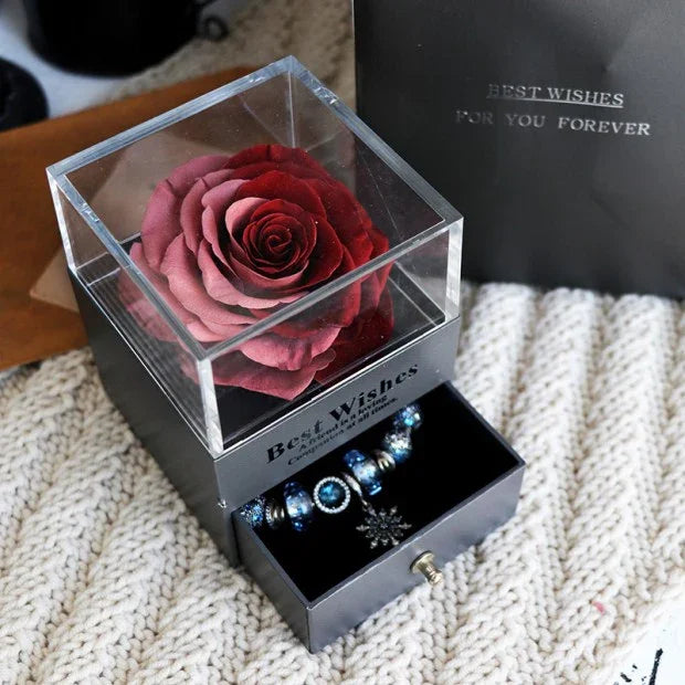 Deep red preserved rose in clear acrylic box with blue charm bracelet drawer on knit fabric