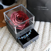Deep red preserved rose in clear acrylic box with blue charm bracelet drawer on knit fabric