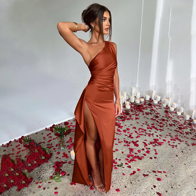 Woman wearing a satin rust-colored one-shoulder gown with high slit, slim fit, surrounded by rose petals.