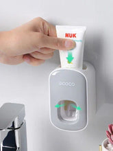 Hand placing toothpaste tube into a wall-mounted automatic toothpaste dispenser in a modern bathroom.