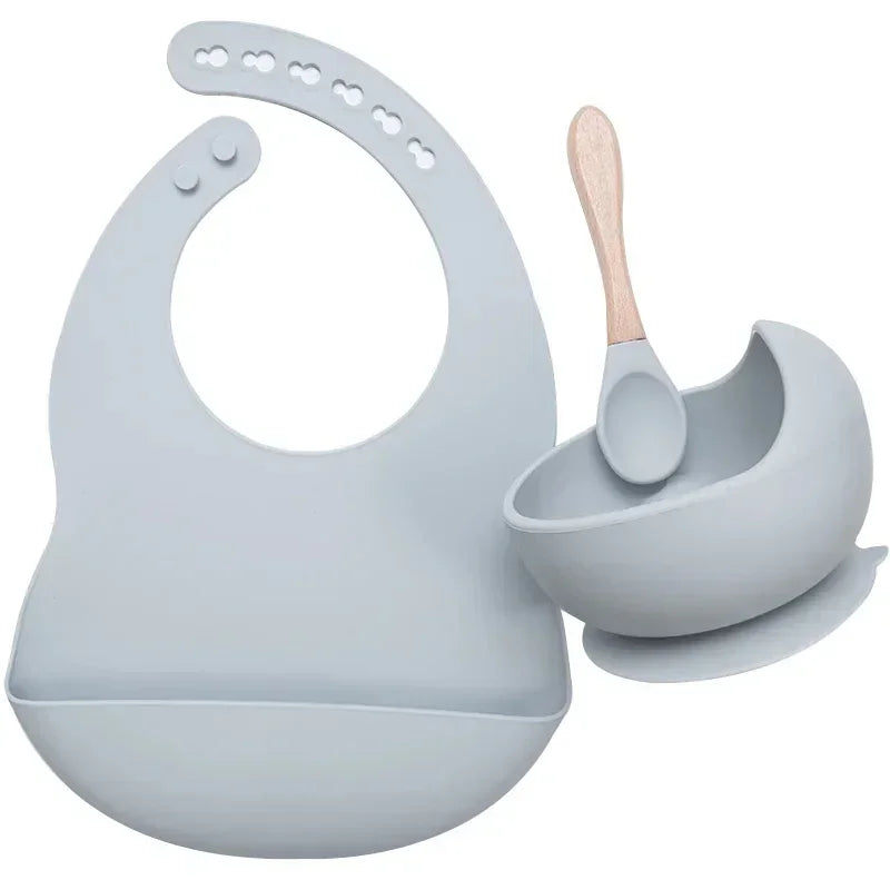 Light grey silicone bib, bowl with suction base, and spoon set for babies.