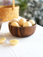Round light-yellow fruits with purple streaks in a dark wooden bowl on a white tablecloth