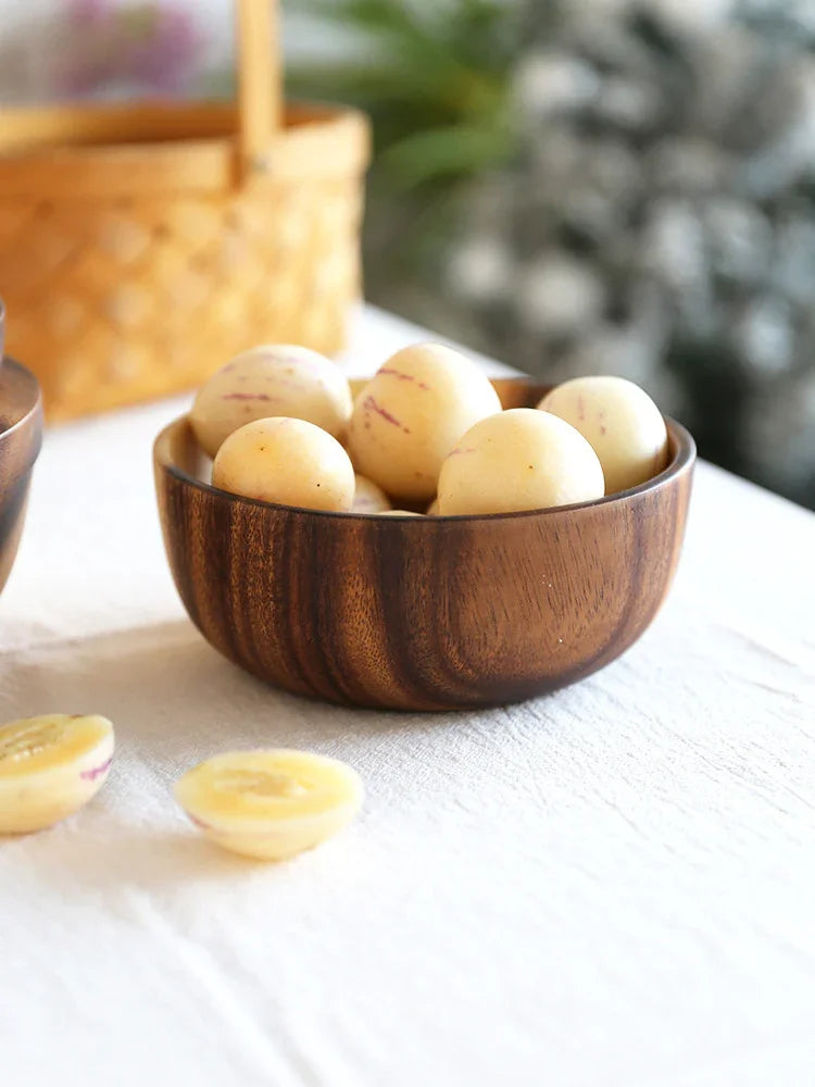 Round light-yellow fruits with purple streaks in a dark wooden bowl on a white tablecloth