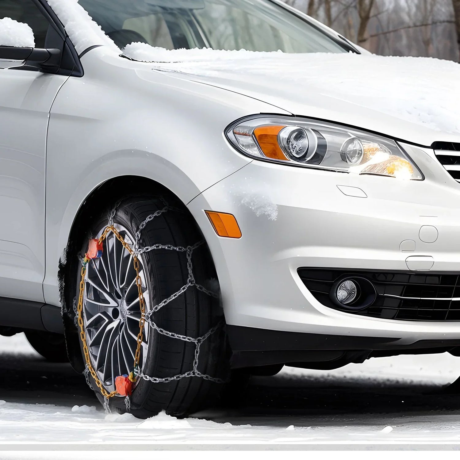 White car with snow tire chains on front wheel, parked on snowy road