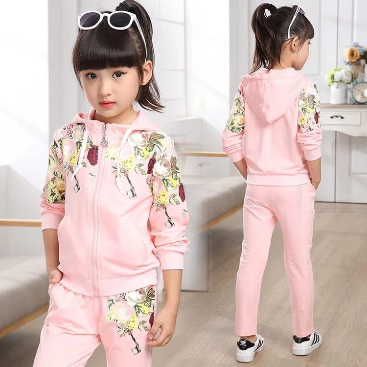 Girl wearing a light pink floral tracksuit set with zip-up hoodie and jogger pants, relaxed fit.
