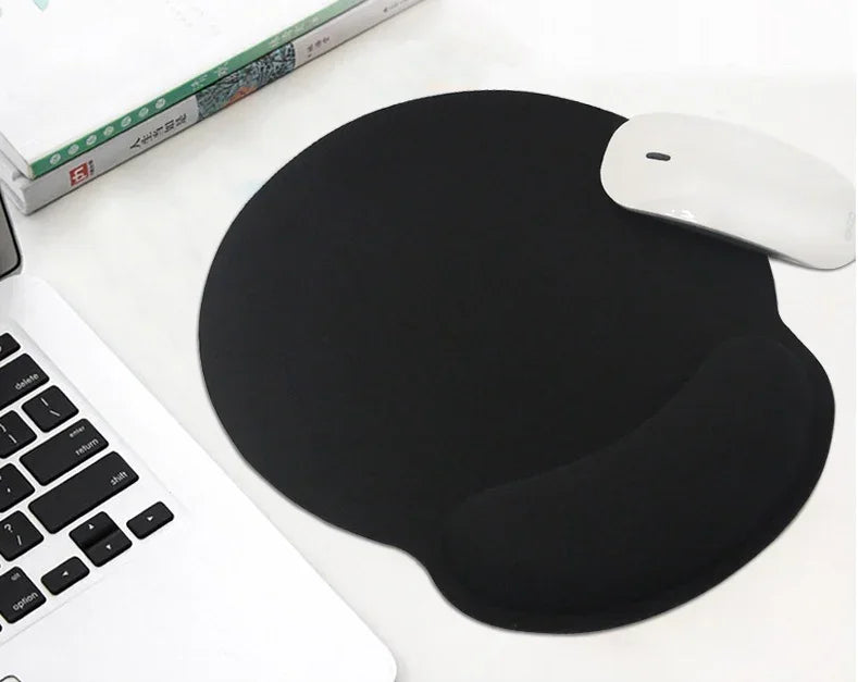 Black ergonomic mouse pad with wrist support on white desk beside laptop and white mouse