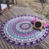 Round mandala tapestry with purple, blue, and white tribal patterns on wooden deck, accented by colorful decorative pillows.
