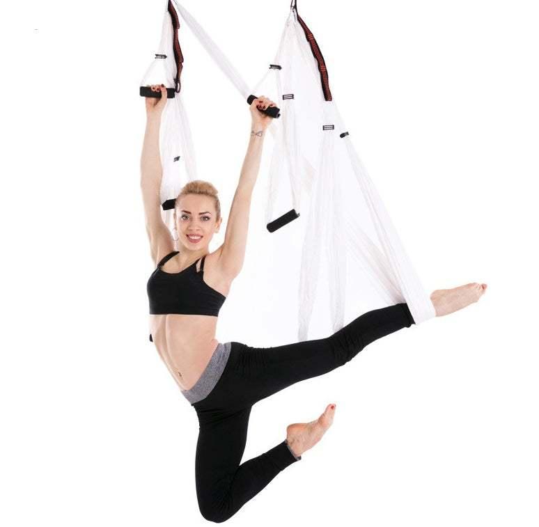 Woman in black athletic crop top and leggings doing aerial yoga in white hammock