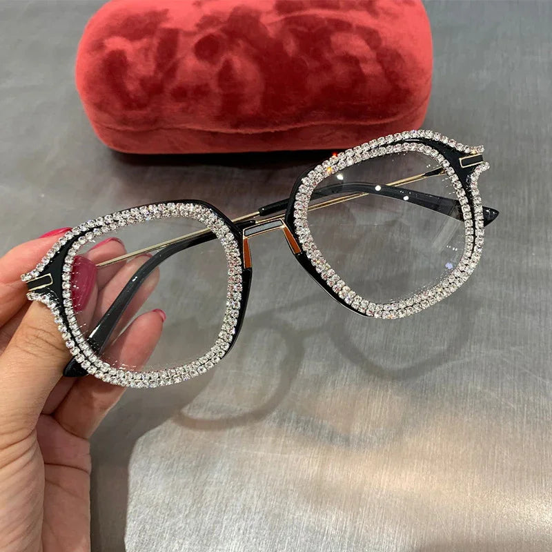 Oversized black square eyeglasses with rhinestone trim and clear lenses, held by hand
