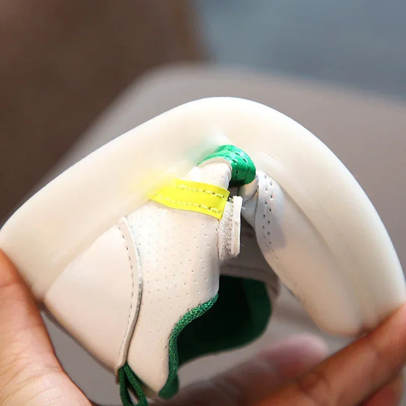 Flexible white sneaker with perforated leather, green trim, and yellow accent, bent in hand