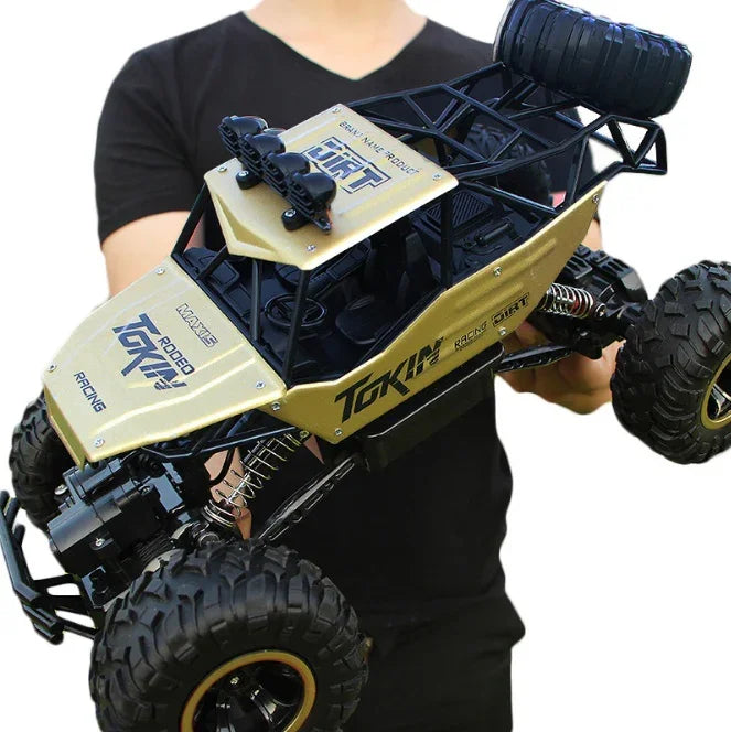 Man holding a gold and black remote control off-road truck with large rugged tires