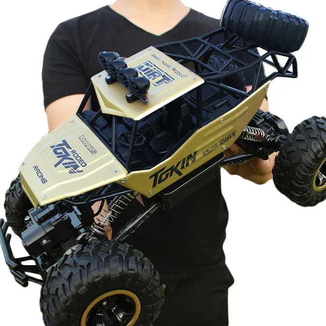 Man holding a gold and black remote control off-road truck with large rugged tires