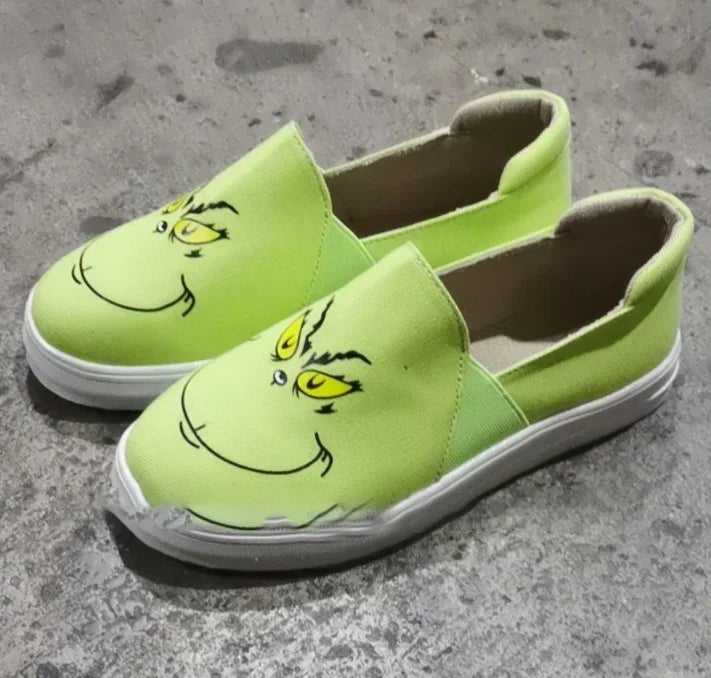 Lime green slip-on canvas shoes with cartoon face print and white rubber soles on a concrete floor.