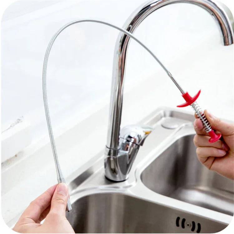 Flexible metal clog remover tool with red handle being used in a kitchen sink drain