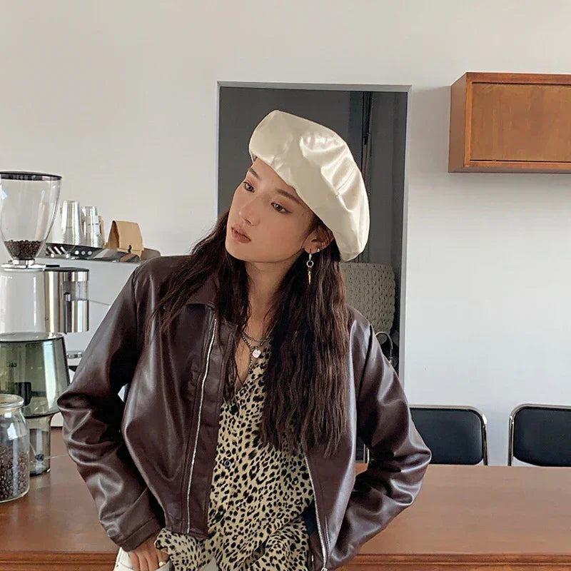 Woman wearing a dark brown faux leather jacket, leopard print blouse, and cream satin beret