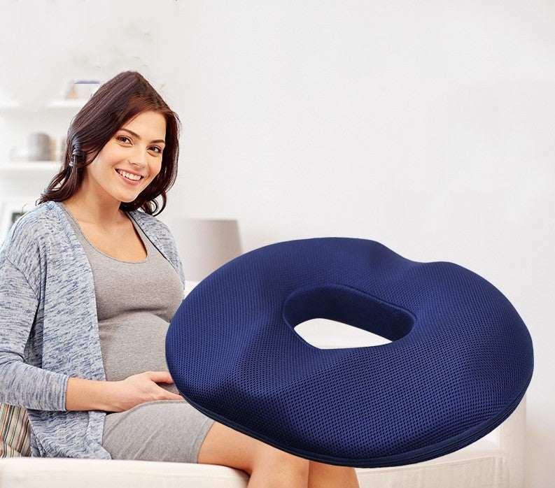 Woman in casual grey dress and blue cardigan seated with a dark blue mesh donut cushion