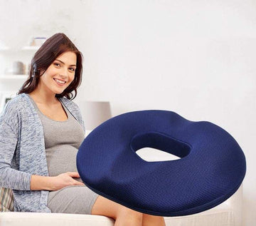 Woman in casual grey dress and blue cardigan seated with a dark blue mesh donut cushion