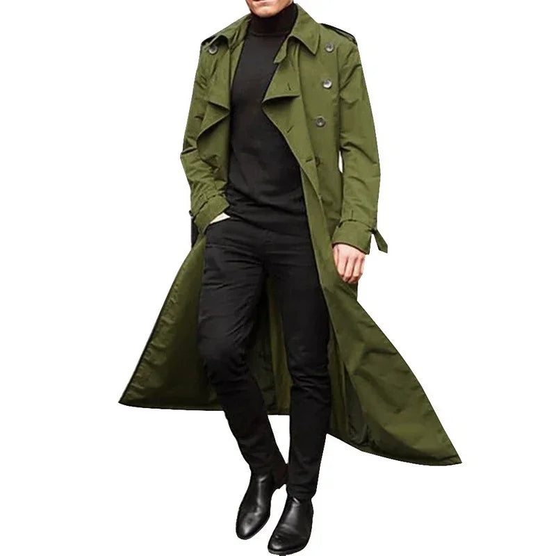 Man wearing a long olive green trench coat, black turtleneck, slim pants, and black boots