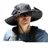 Man wearing wide-brim camo sun hat with solar fans, blue athletic shirt, and sunglasses.