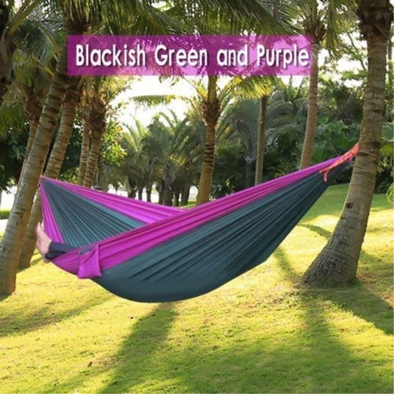 Blackish green and purple nylon hammock hanging between palm trees outdoors.