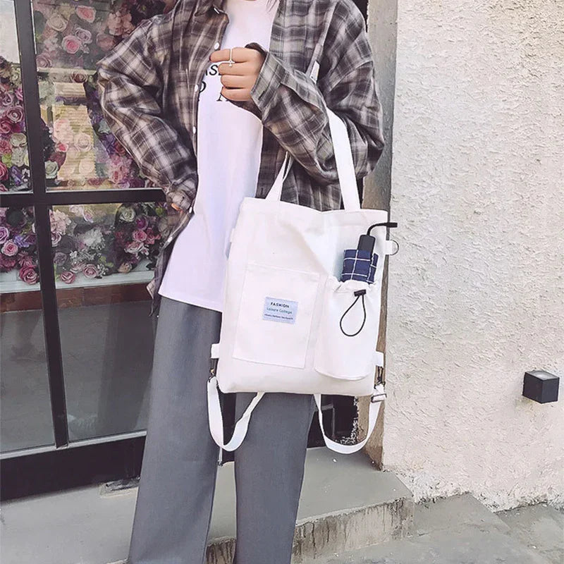 Casual streetwear look with a plaid shirt, white t-shirt, grey wide-leg pants, and a white canvas tote bag.