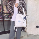 Casual streetwear look with a plaid shirt, white t-shirt, grey wide-leg pants, and a white canvas tote bag.