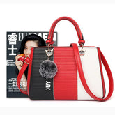 Color block handbag in black, red, and white faux leather with gold accents and pom-pom charm