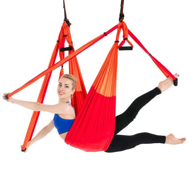 Woman in blue sports bra and black leggings using red aerial yoga swing, performing a split