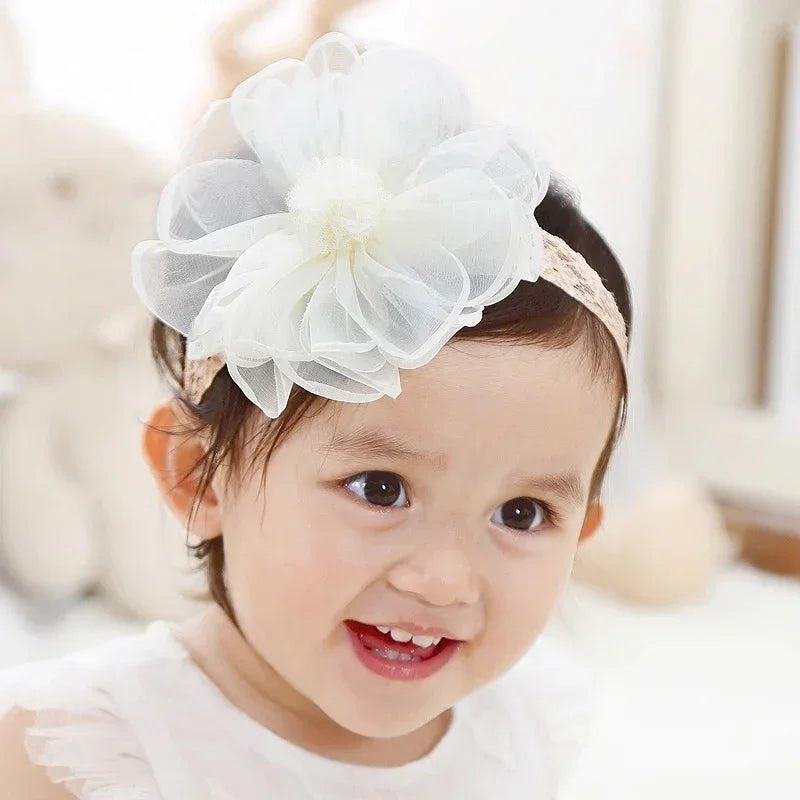 Baby wearing a white sheer flower headband and white sleeveless top, soft background