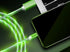 Green LED charging cables connected to a smartphone and laptop on dark background