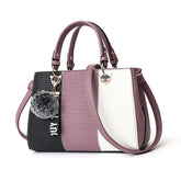 Colorblock handbag in black, mauve, and white faux leather with gold hardware and pom-pom charm