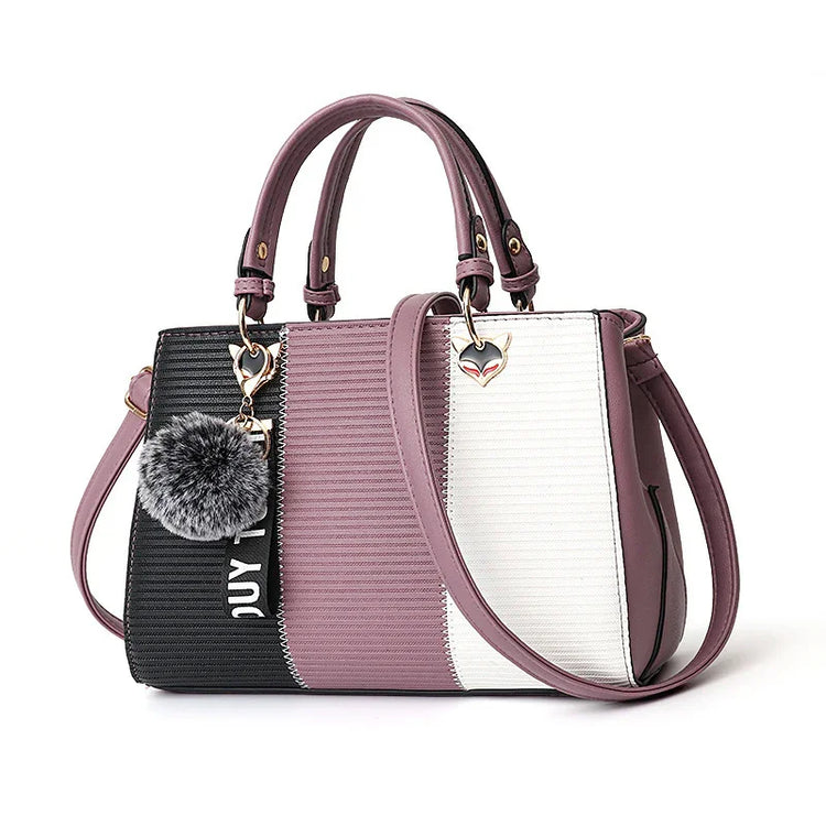 Colorblock handbag in black, mauve, and white faux leather with gold hardware and pom-pom charm