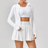 Woman wearing white athletic zip jacket, crop top, and pleated tennis skirt set