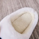 Close-up of white faux fur slipper with plush fleece lining on a carpeted floor