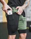 Olive green and black athletic shorts with side pocket, stretchy fit, showing phone storage