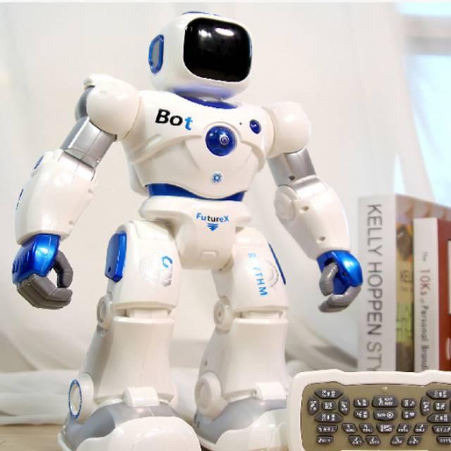 White and blue plastic toy robot with remote control on a desk, books in background.