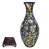 Tall ceramic vase with blue background and yellow floral pattern, next to wooden stand