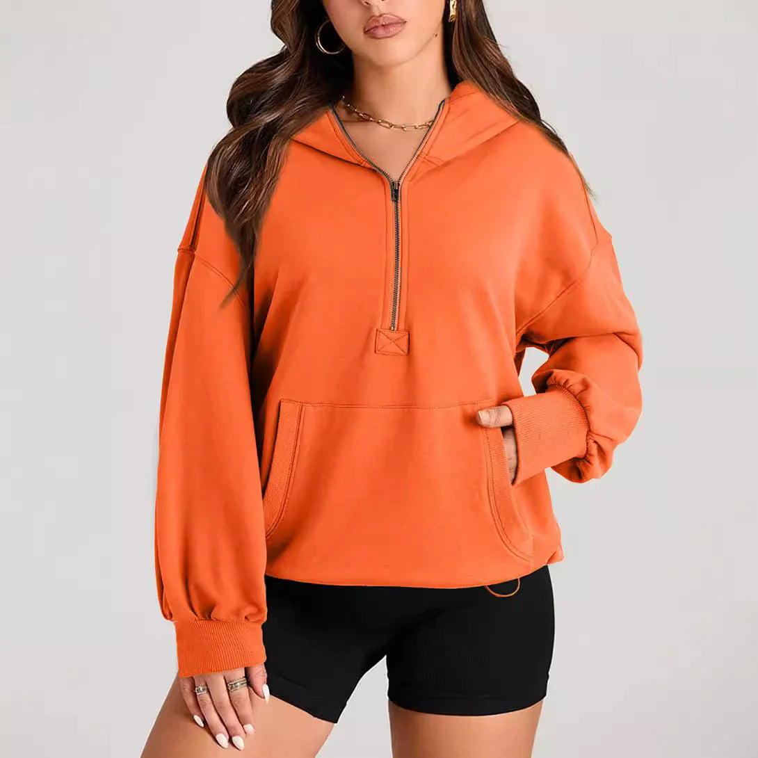 Woman wearing an orange pullover hoodie with front pocket and half-zip, paired with black shorts
