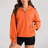 Woman wearing an orange pullover hoodie with front pocket and half-zip, paired with black shorts